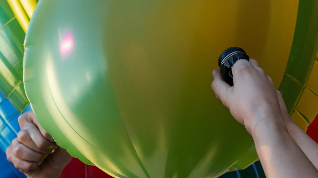 Primer plano de manos con inflador manual de globos y bocetos de diseño al fondo, parte del aprendizaje técnico de un curso de decoración